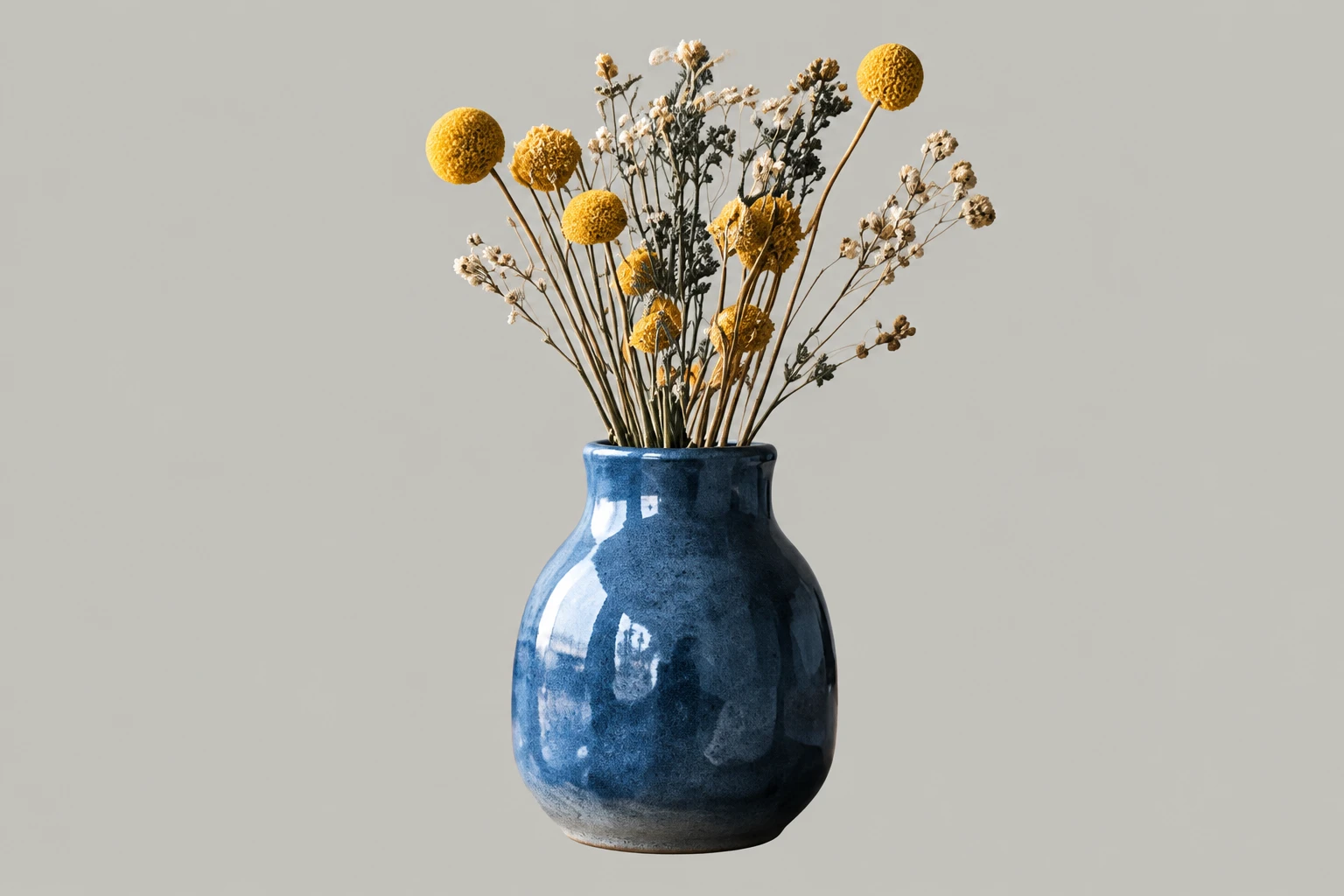 Blauwe vaas met gele droogbloemen op een bureau in een kantoor